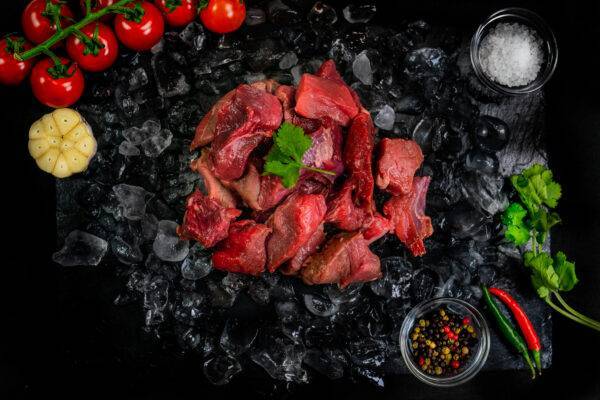 diced beef stewing steak on a bed of ice next to garnishes