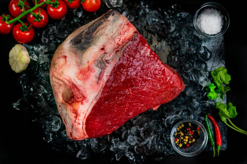 a cut of beef topside on a bed of ice surrounded by veg