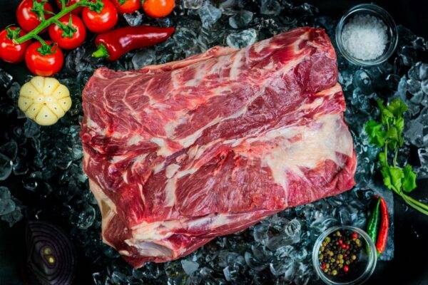 cut of lamb shoulder on a pile of ice surrounded by seasonings