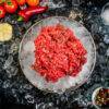 pile of beef steak mince in a bowl of ice on a bed of ice surrounded by garnish