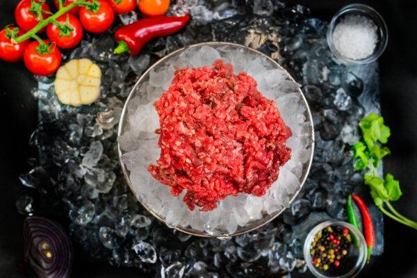 pile of beef steak mince in a bowl of ice on a bed of ice surrounded by garnish