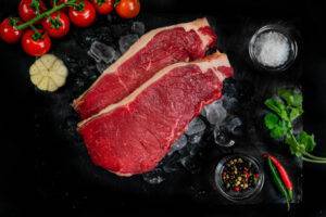 2 cuts of sirloin steak on a bed of ice, surrounded by garnishes and seasonings