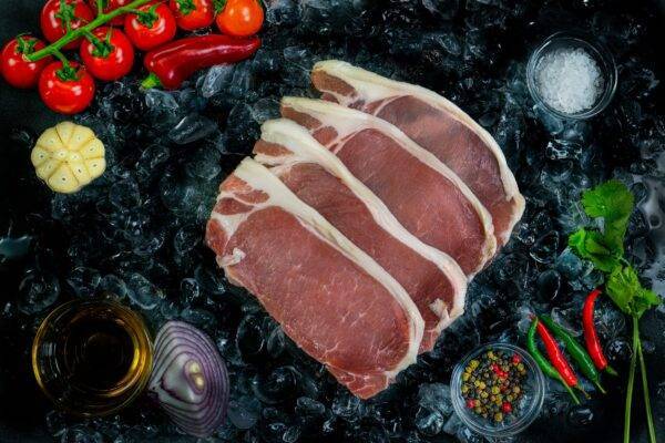 4 slices of dry cured pork on a bed of ice surrounded by veg