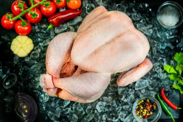 whole chicken laying on a bed of ice, surrounded by veg and seasonings