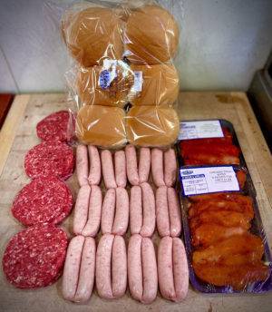 a display of burgers, sausages, chicken tikka and burger buns on a wooden board